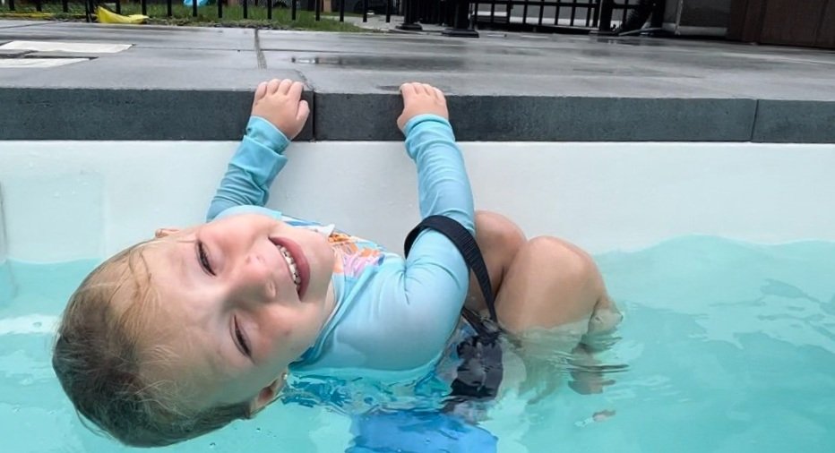 Un jeune garçon s'accroche en souriant au bord de la piscine