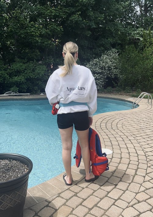 Une monitrice pose devant une piscine avec un chandail personnalisé au logo d'AquaStars