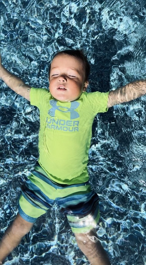 Un jeune enfant apprend à flotter sur le dos dans son costume de bain vert fluo et bleu lors d'un cours de natation à domicile
