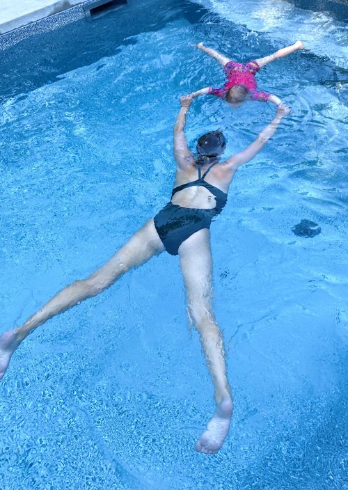 Une monitrice aquatique apprend à une jeune fille à flotter dans l'eau lors d'un cours de natation à domicile pour enfants