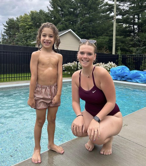 Un jeune garçon pose avec sa monitrice au bord d'une piscine creusée