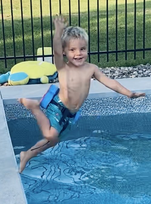 Un jeune garçon au maillot de bain rayé bleu et noir saute dans une piscine creusée avec un flotteur lors d'un cours de natation à domicile